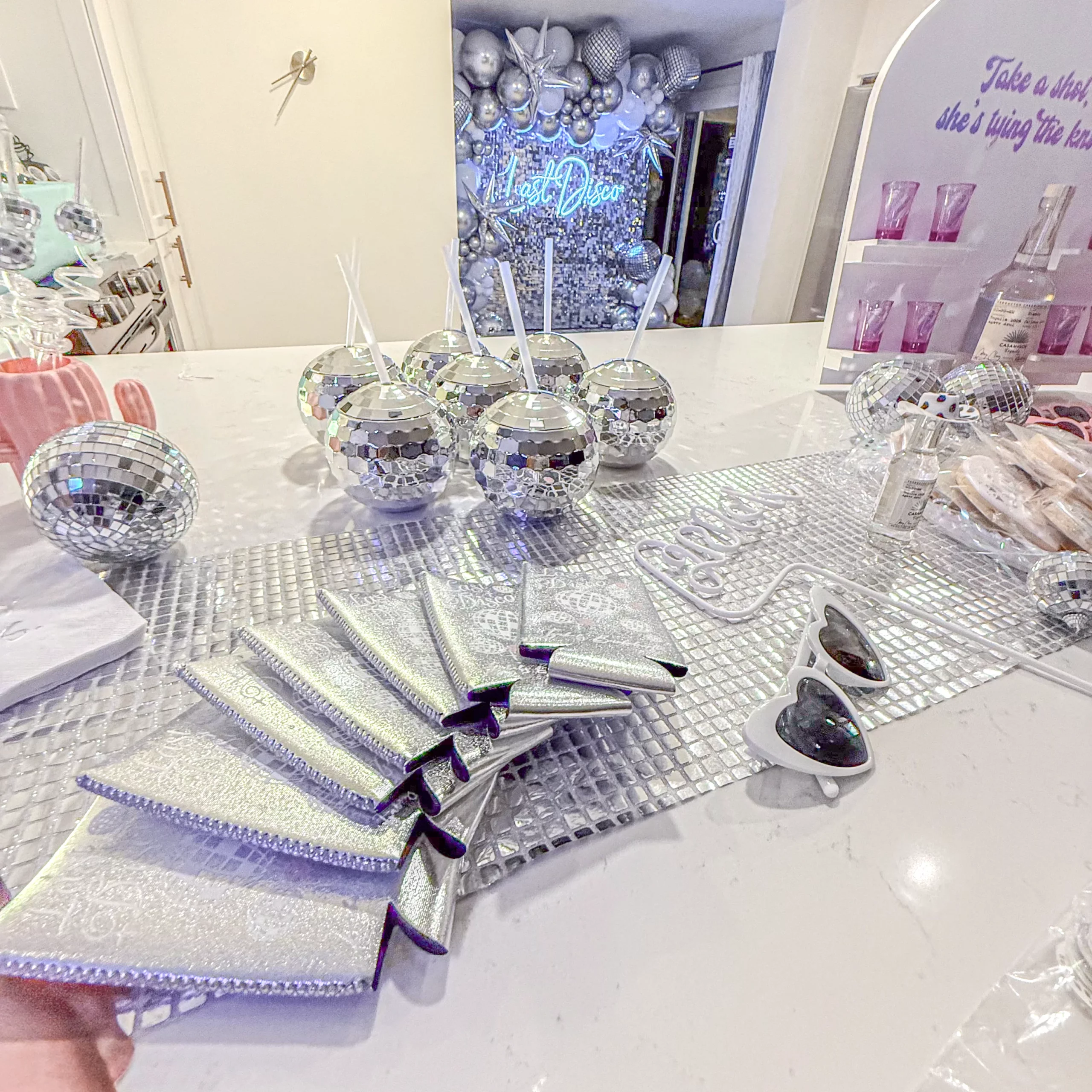 Last Disco bachelorette table setup with disco ball tumblers, neon sign, custom koozies, and themed details