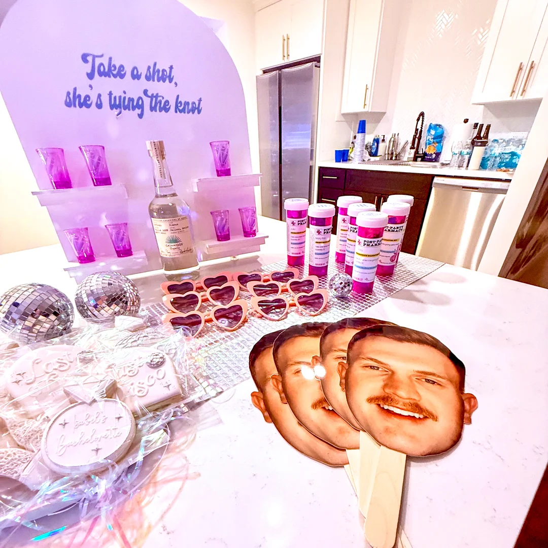Last Disco bachelorette table setup with face fans, neon sign, sunglasses, custom last disco cookies and themed details