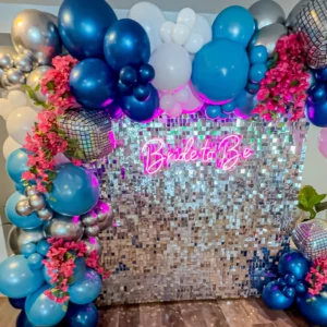 Mamma Mia bachelorette backdrop with silver shimmer wall, blue and white balloon garland, pink bougainvillea florals, disco balls, and Bride to Be neon sign