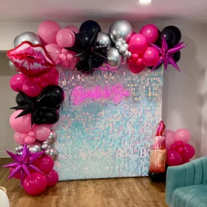 Mean Girls bachelorette backdrop with iridescent shimmer wall, pink and black balloon garland, lips mylar balloon, and Bride to Be neon sign